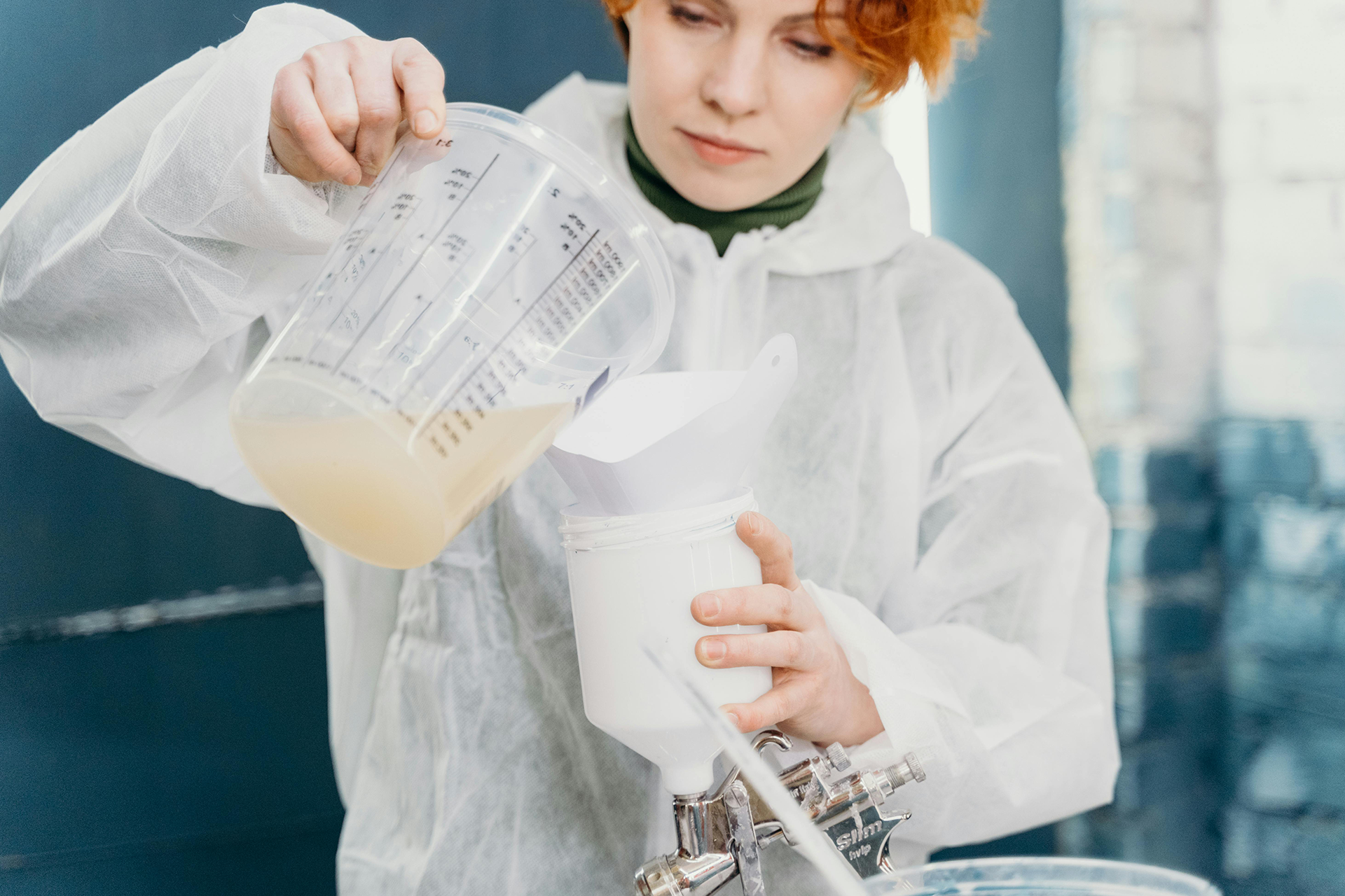 Welche Grundierung für 2K Strukturlack? Die Basis für den Protector Person in weißem Schutzanzug gießt Grundierung für Lack aus einem Messbecher in einen weißen Behälter